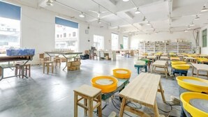 Et rummeligt klasseværelse med borde, stole, store vinduer og reoler fyldt med bøger og undervisningsmaterialer.
