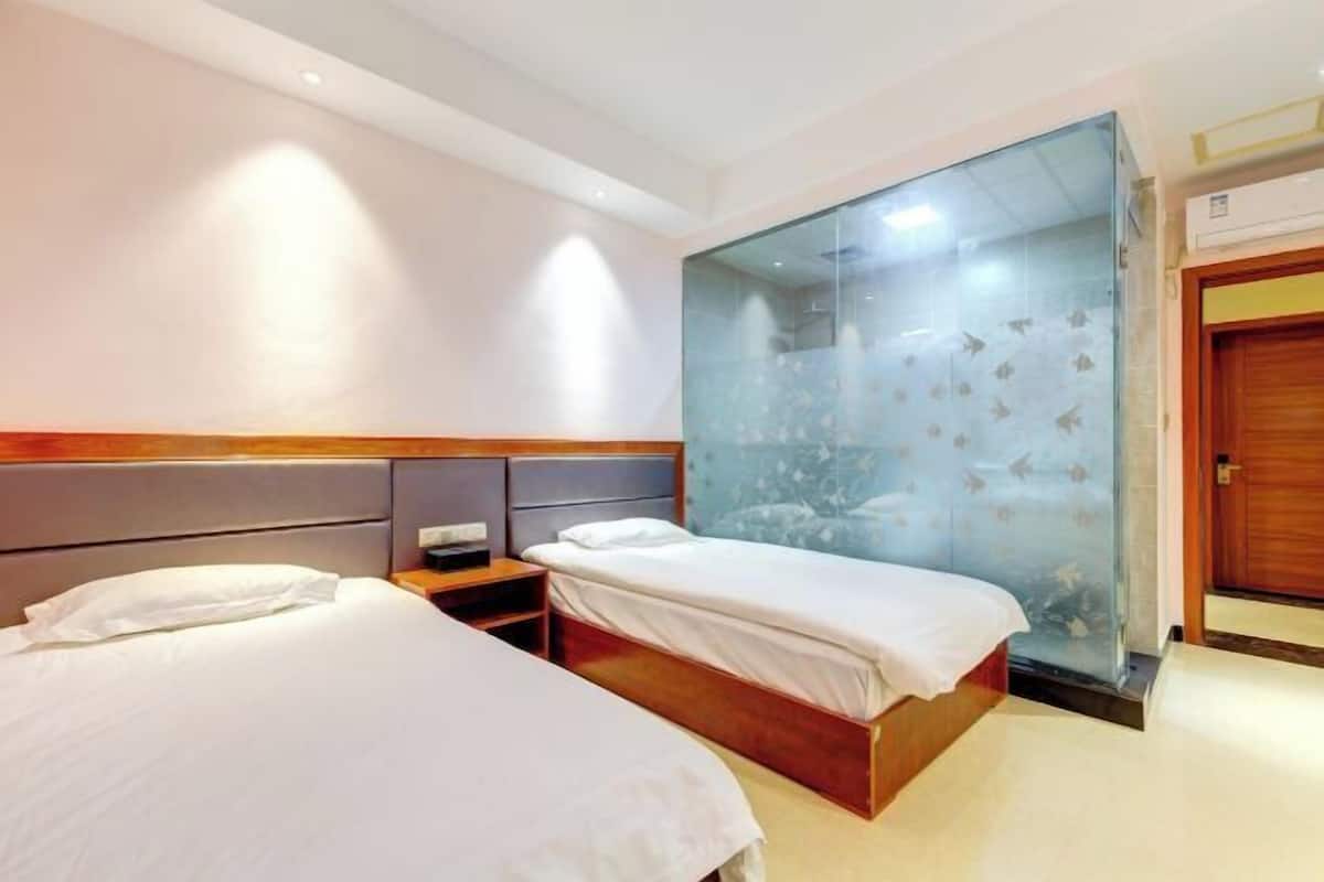 A hotel room with two beds, a wooden headboard, a nightstand, and a glass partition with a fish pattern.