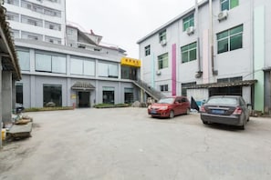 A building with a staircase leading to an entrance, a parking area with two cars, and a large vertical structure. - Very Much Pottery Homestay (Fuliang)