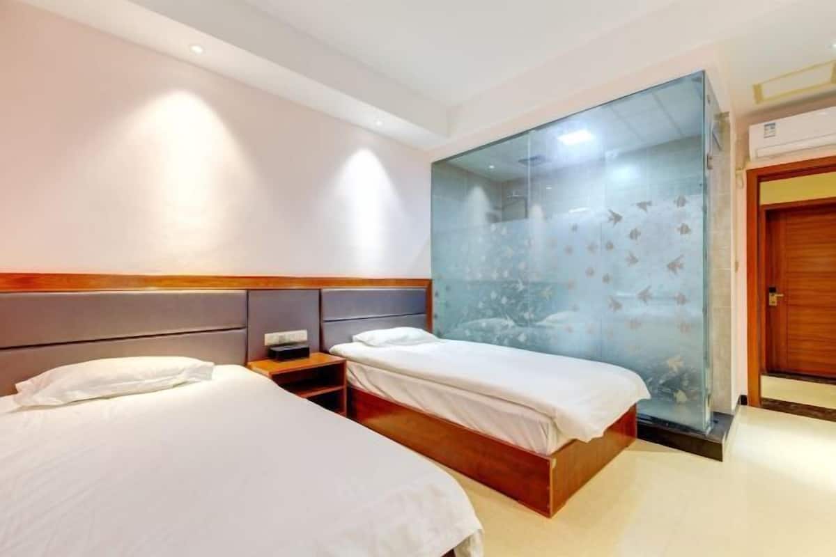 A hotel room with two beds, a wooden headboard, a nightstand, and a glass partition with a cityscape view.
