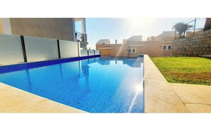 A swimming pool with a clear blue water surface, surrounded by a concrete deck and a stone wall.