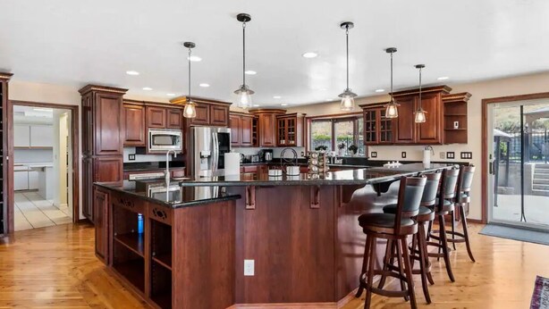 Una cocina amplia con armarios de madera, una isla central con taburetes de bar e iluminación colgante.