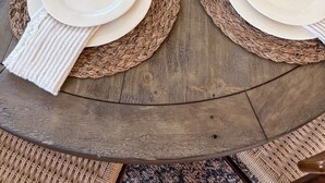 A round wooden dining table set with white plates, brown placemats, and clear wine glasses. - Chic wine country cottage and garden (Healdsburg)