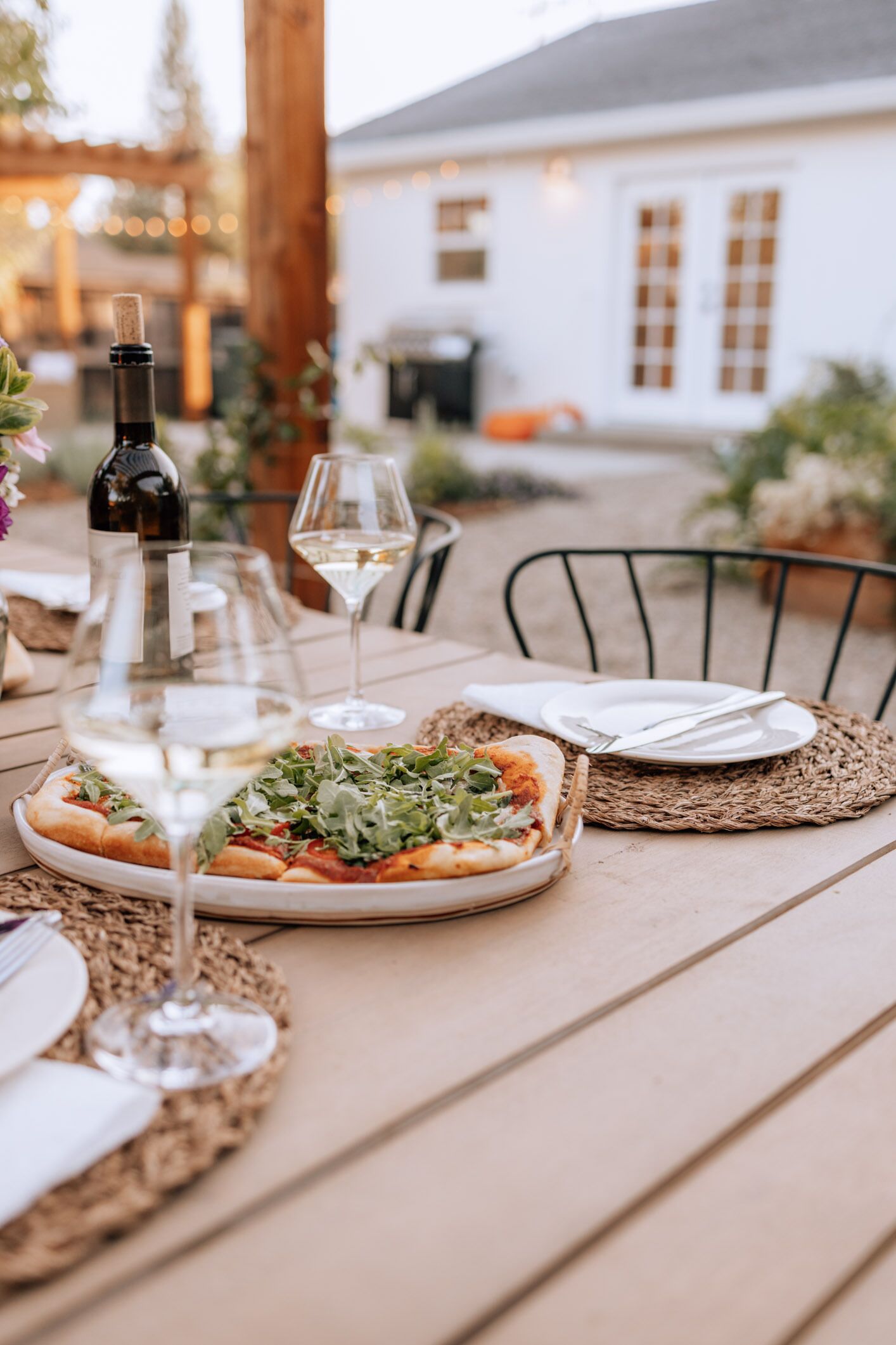 A dining table set with a pizza, wine glasses, and a bottle of wine.