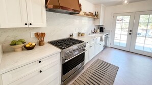 A modern kitchen with white cabinets, a stainless steel stove, and a large window. - Chic wine country cottage and garden (Healdsburg)