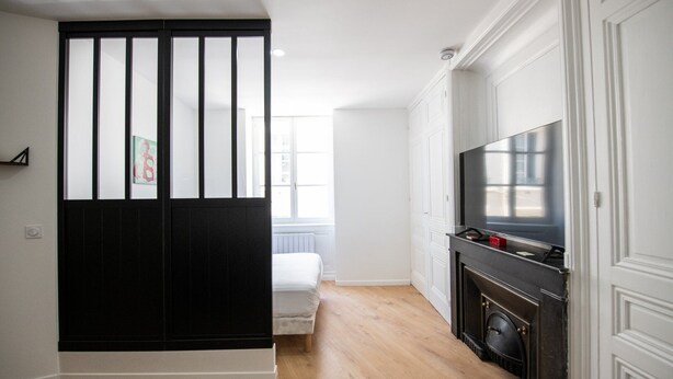 A modern kitchen with a black and white color scheme, a built-in stove, and a large flat-screen TV. - L'Arty-Beautiful well-furnished 31m² flat in Valmy (Lyon)
