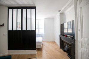 A modern kitchen with a black and white color scheme, a built-in stove, and a large flat-screen TV. - L'Arty-Beautiful well-furnished 31m² flat in Valmy (Lyon)