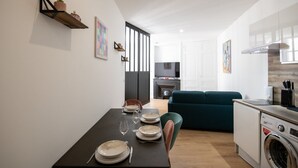 A modern kitchen with a built-in washing machine, a dining area with a table set for four, and a living area with a sofa and a TV. - L'Arty-Beautiful well-furnished 31m² flat in Valmy (Lyon)