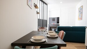 A dining area with a table set for four, a teal sofa, and a television in the background. - L'Arty-Beautiful well-furnished 31m² flat in Valmy (Lyon)