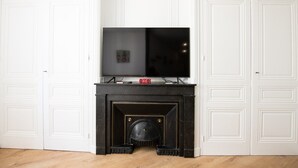 A room with a fireplace, a television mounted above it, and white doors on either side. - L'Arty-Beautiful well-furnished 31m² flat in Valmy (Lyon)