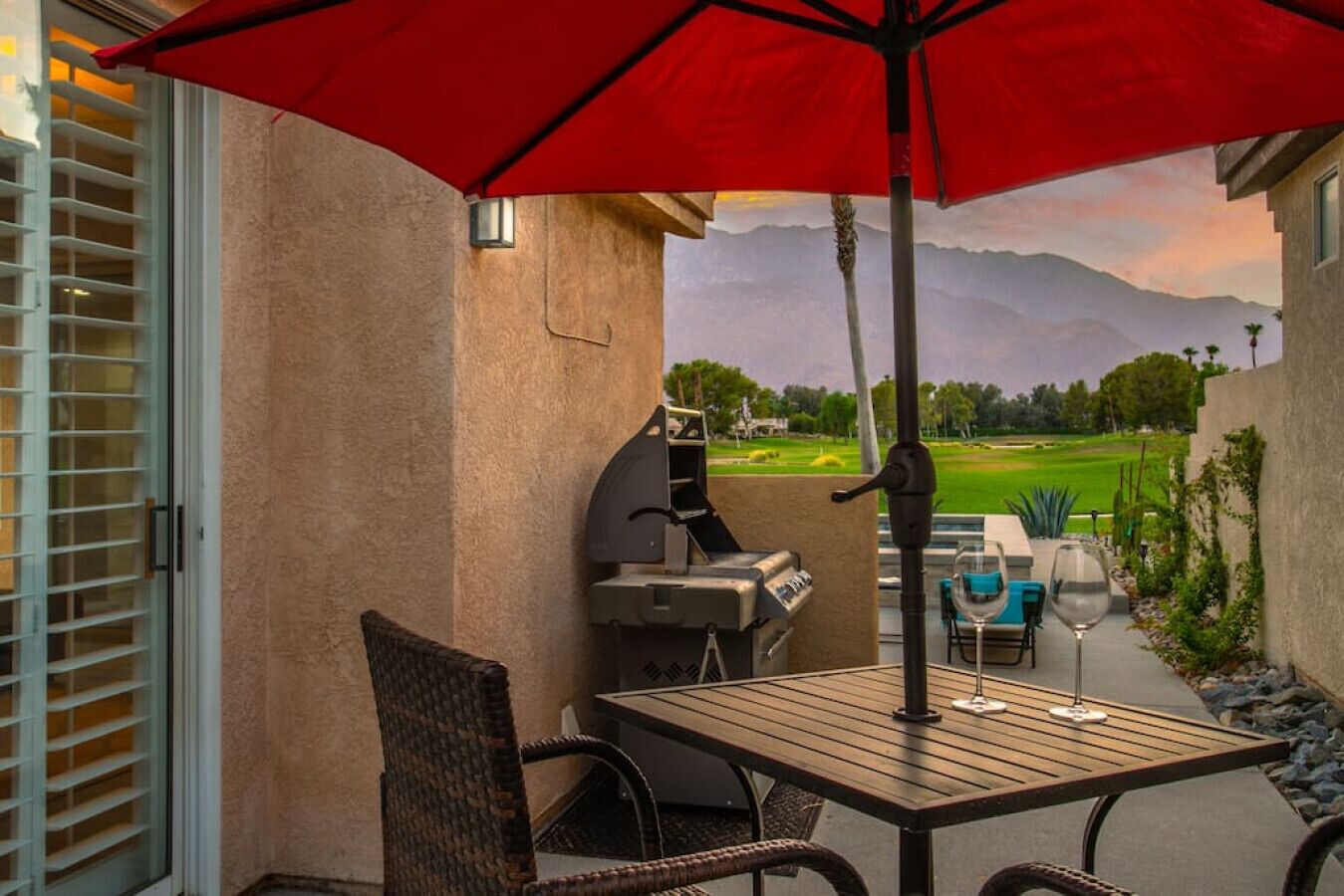 Eine Terrasse im Freien mit Tisch, Stühlen, einem Grill und einem roten Sonnenschirm.