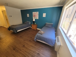 Two single beds with matching bedspreads and pillows, a nightstand with a lamp, and framed pictures adorn this cozy room.