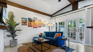 A living room with a blue sofa, a coffee table, a potted plant, and a large window with a view of the outdoors.