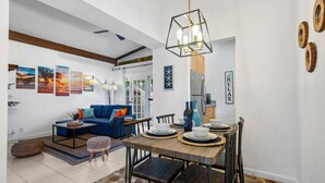 A modern living room with a blue sofa, a dining table set with plates, and a hanging light fixture.