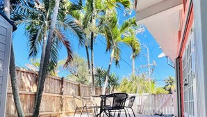 A wooden deck with a table and chairs, surrounded by a wooden fence and palm trees.