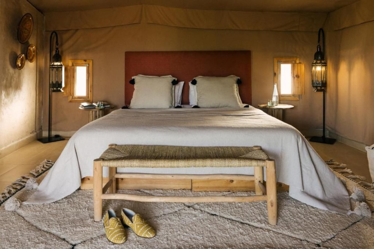 Une chambre avec un grand lit, deux tables de chevet, un banc et un tapis.