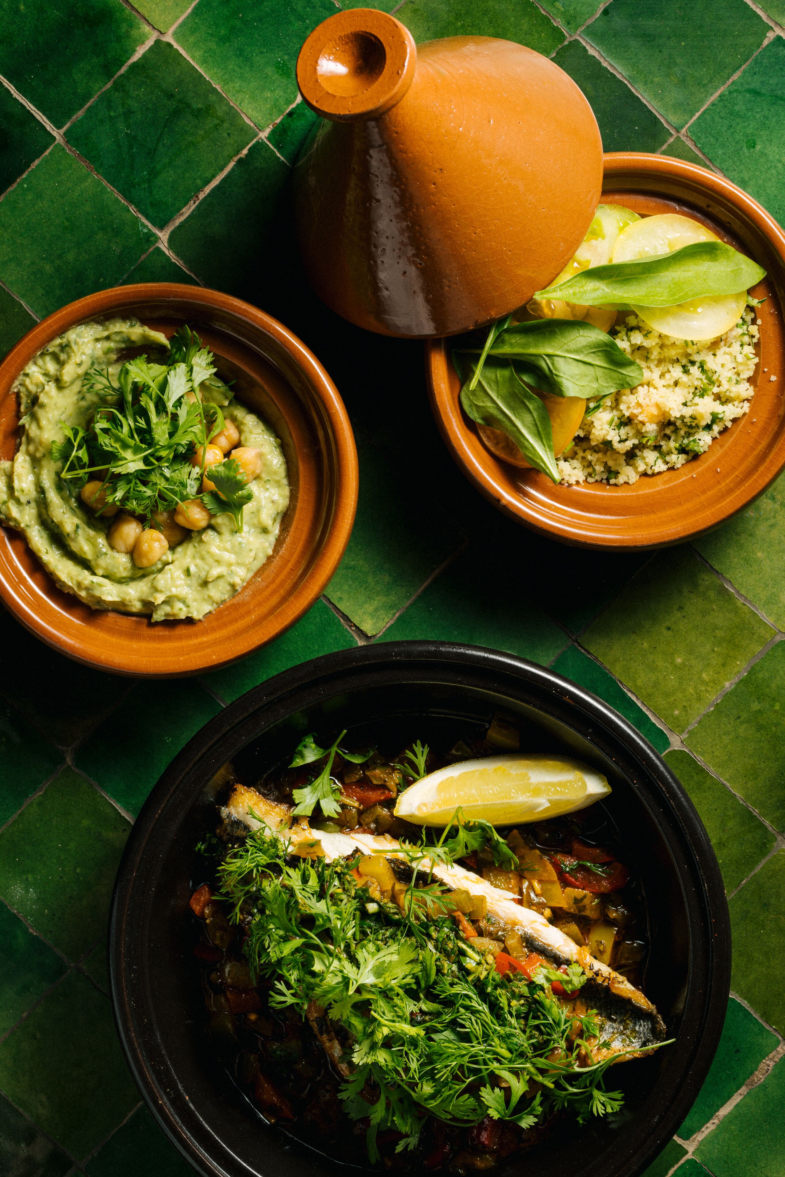 Ein Tisch mit drei Gerichten: eine Schüssel Guacamole, eine Schüssel Kuskus mit Gemüse und eine Schüssel Fisch mit Gemüse.