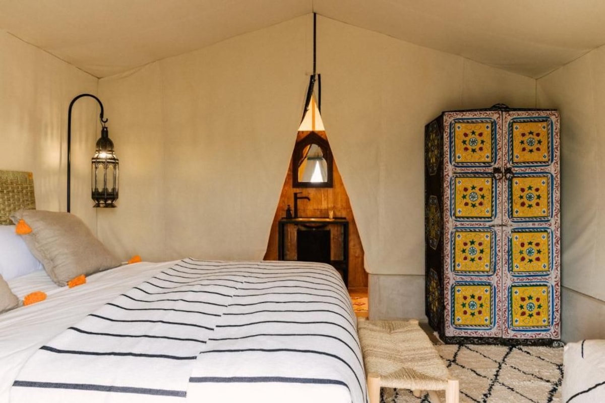 Une chambre à coucher avec un lit, une lanterne suspendue, une armoire à motifs et un petit tabouret en bois.