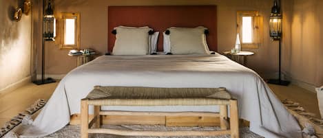 A bedroom with a large bed, two bedside tables, a bench, and a pair of slippers.