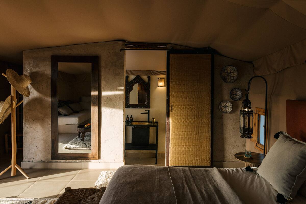 Une chambre à coucher comprenant un lit, une table de chevet, un miroir, un luminaire suspendu et une vue sur une autre pièce.