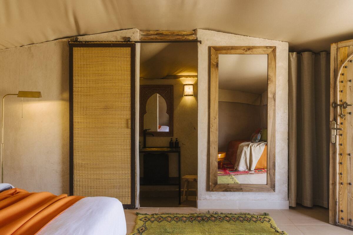 Une pièce comprenant un lit, un miroir, une petite table et une porte donnant sur une autre pièce.