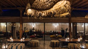 An indoor lounge area with a thatched ceiling, wooden furniture, and ambient lighting. - Caravan Agafay by Our Habitas (Agafay)