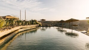 An infinity pool with a view of the desert, surrounded by lounge chairs and umbrellas. - Caravan Agafay by Our Habitas (Agafay)