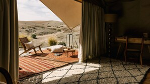 A tent with a view of a desert landscape, a small table with a lamp, and a chair with cushions. - Caravan Agafay by Our Habitas (Agafay)