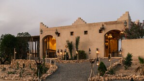 Un bâtiment à la façade de style désertique, doté d’arcades et d’un chemin de gravier menant à l’entrée.