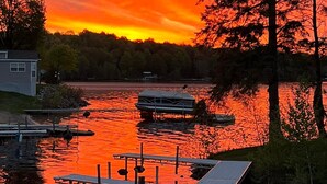 Laituri, jossa on vene, talo ja metsäinen alue vesistön äärellä auringonlaskun aikaan.