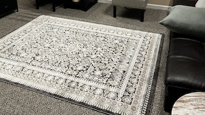 A living room with a patterned rug, a dark wooden desk, a grey armchair, a round wall clock, and a small table with a remote control. - Comfortable, convenient 2BR 2BA apt in Alameda (Alameda)