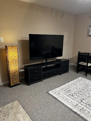 Ein Wohnzimmer mit Flachbildfernseher, einer schwarzen Unterhaltungsecke, einem gemusterten Teppich und einer hohen, beleuchteten Skulptur.