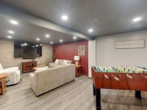 A cozy room with a sofa, a foosball table, a TV, and a wall-mounted sign.