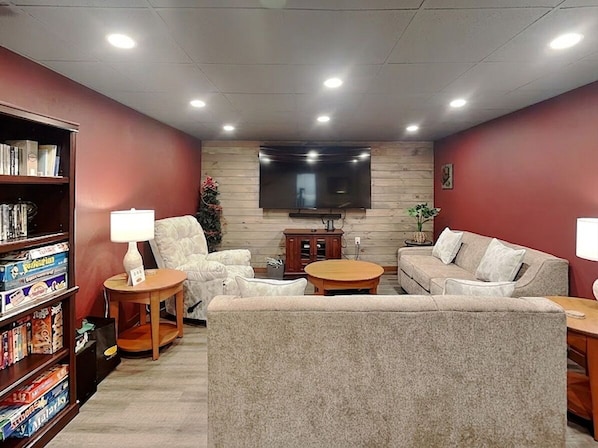 A living room with a flat-screen TV, two sofas, a coffee table, a bookshelf, and a lamp.