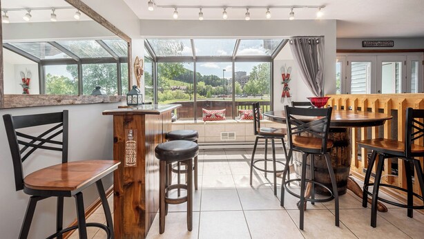 A dining area with a wooden bar, multiple chairs, and a large window offering a view of the outdoors.