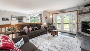 A cozy living room with a fireplace, a large window, and a sliding glass door leading to a deck.