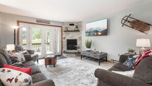 A cozy living room with a fireplace, comfortable seating, and a view of the outdoors.