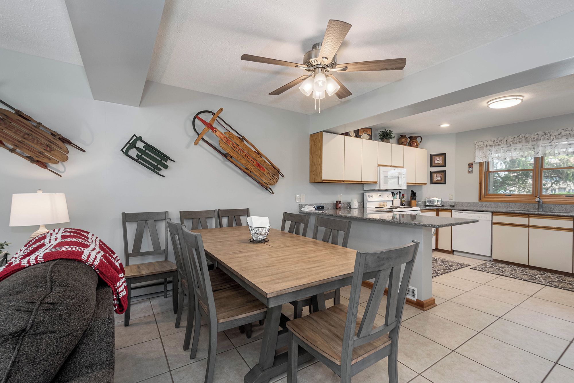 A modern kitchen with a dining area, featuring a ceiling fan, wooden cabinets, and a large island with a built-in microwave.