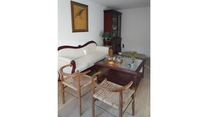 A living room with a white sofa, two wooden chairs with woven seats, a glass coffee table with decorative items, a dark wooden cabinet, and a framed picture on the wall. - HOLIDAY BEACH VACATIONS (El Puerto de Santa María)