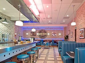 A restaurant with a bar area, blue booths, and a brick wall with a 'Hamburgers' sign.