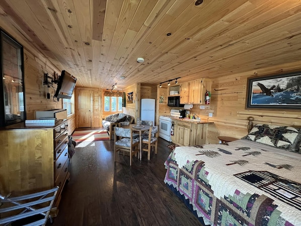 L’intérieur chaleureux d’un chalet avec un plafond en bois, un coin repas, une cuisine et un lit recouvert d’une courtepointe.