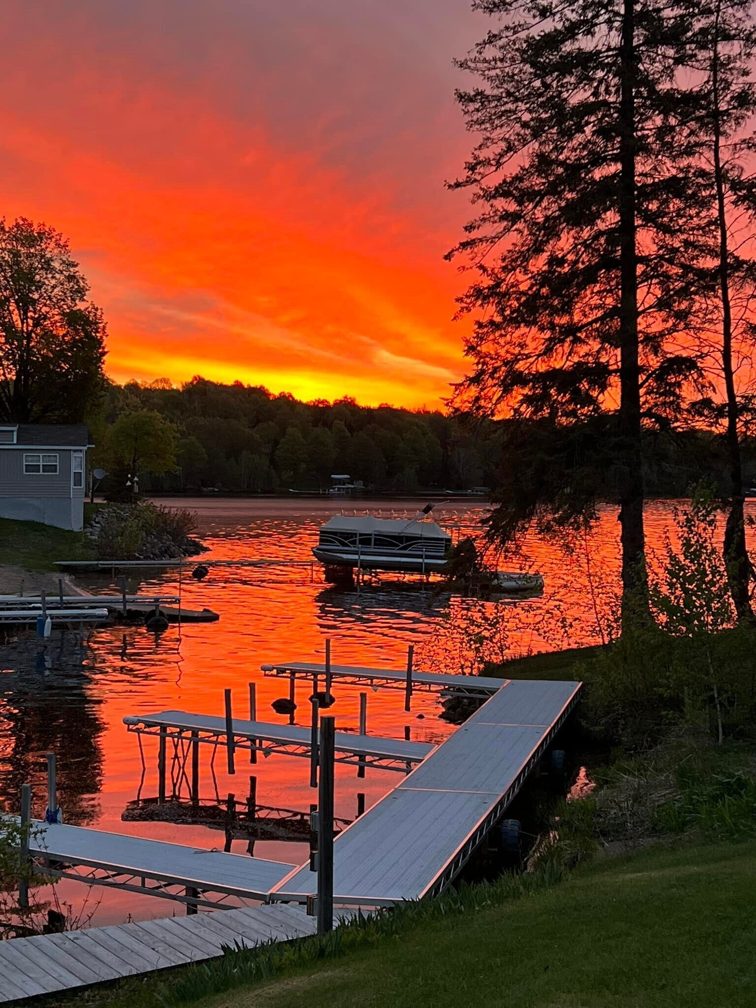 Um cais com um barco, uma casa e uma área arborizada à beira de um corpo d'água durante o pôr do sol.