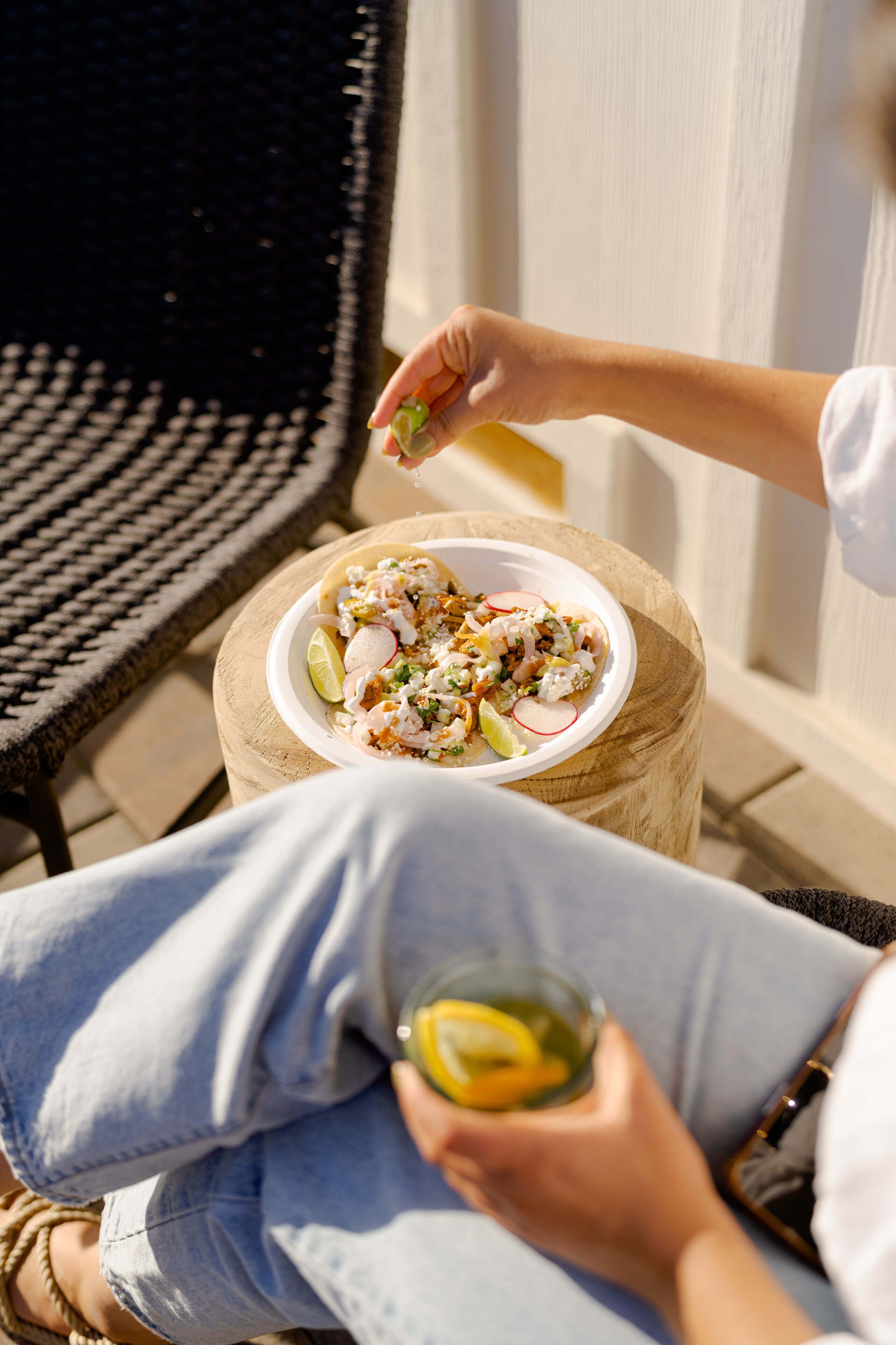 A person sitting on a chair outdoors with a plate of food and a drink.
