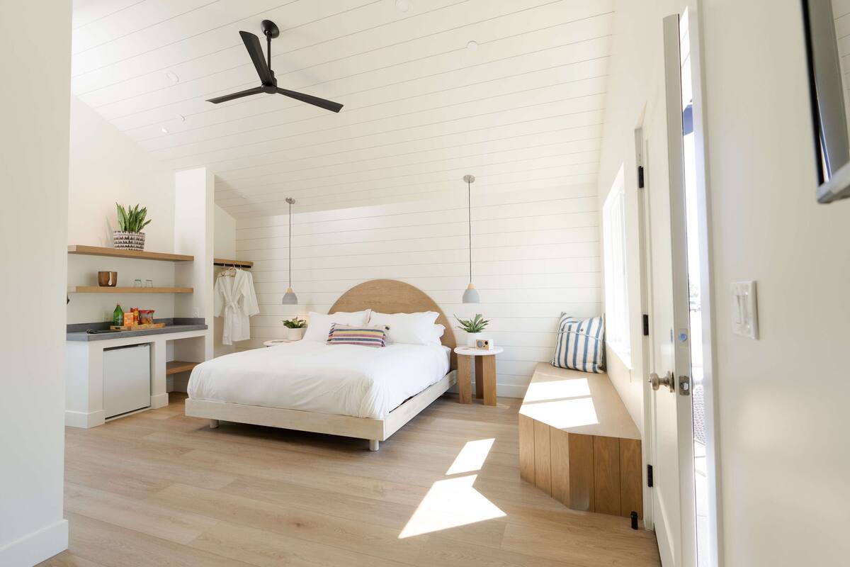 A modern bedroom with a bed, bedside tables, a desk, and a ceiling fan.