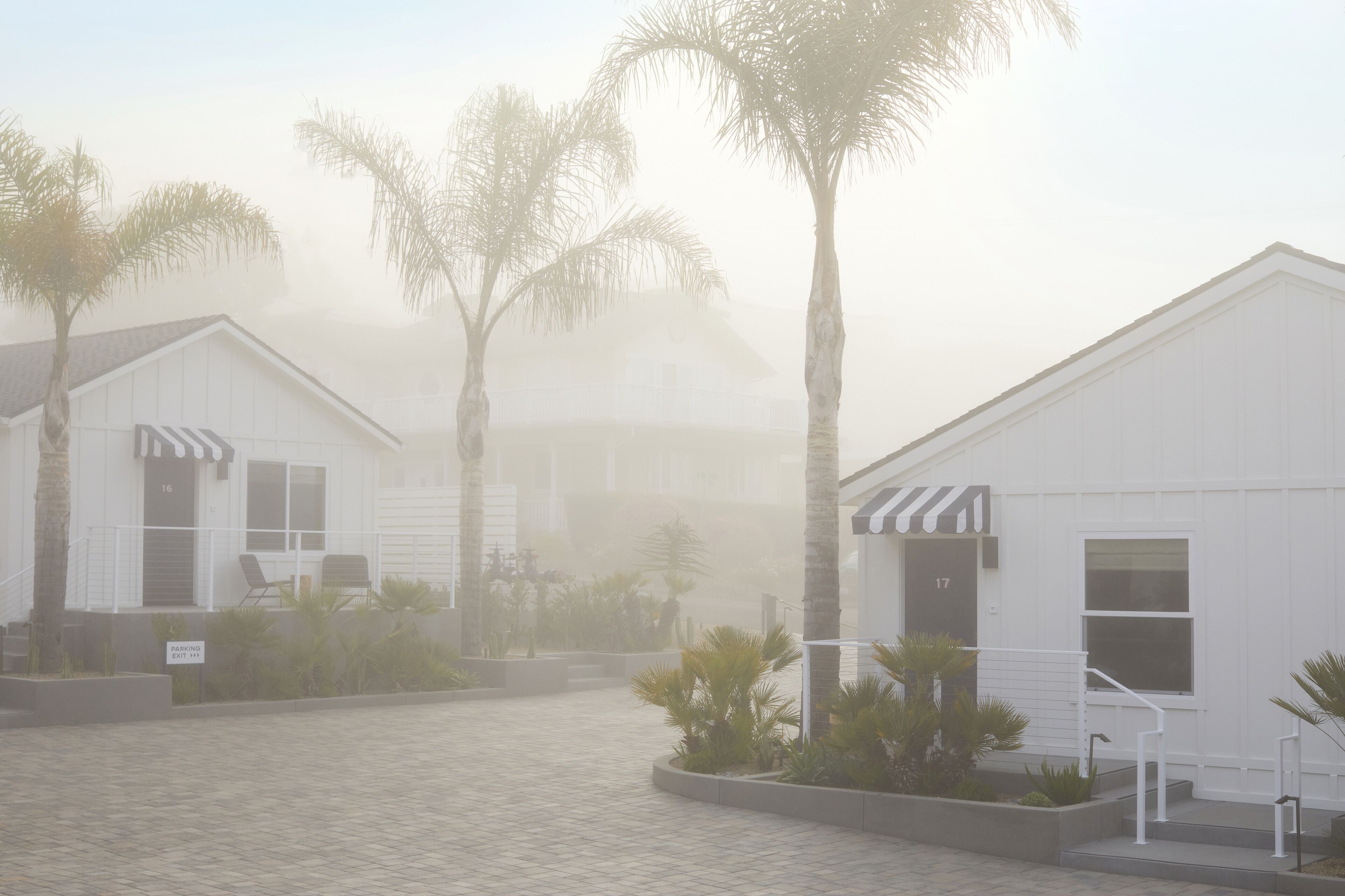 A building with a white exterior, numbered doors, and a paved entrance area with palm trees.