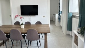 Ein moderner Essbereich mit einem Holztisch, vier Stühlen, einer Topforchidee und einem flachbildfernseher an der Wand.