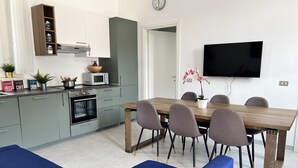 Eine moderne Küche mit Mikrowelle, Backofen und Schränken. Ein Esstisch mit Stühlen und ein an der Wand befestigtes Fernsehgerät.