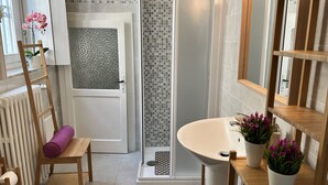 Ein Badezimmer mit Dusche, Waschbecken, Spiegel und einem Holzstuhl mit Kissen.