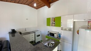 A compact kitchen with a stove, microwave, and refrigerator, featuring green and white cabinets. - Villa 209 sua casa em Campos do Jordão (Campos do Jordão)