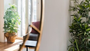 A room with a large window, a wooden floor, a black sofa with a red cushion, and two potted plants. - GuestReady - Bright Apartment near Bolhão (Porto)